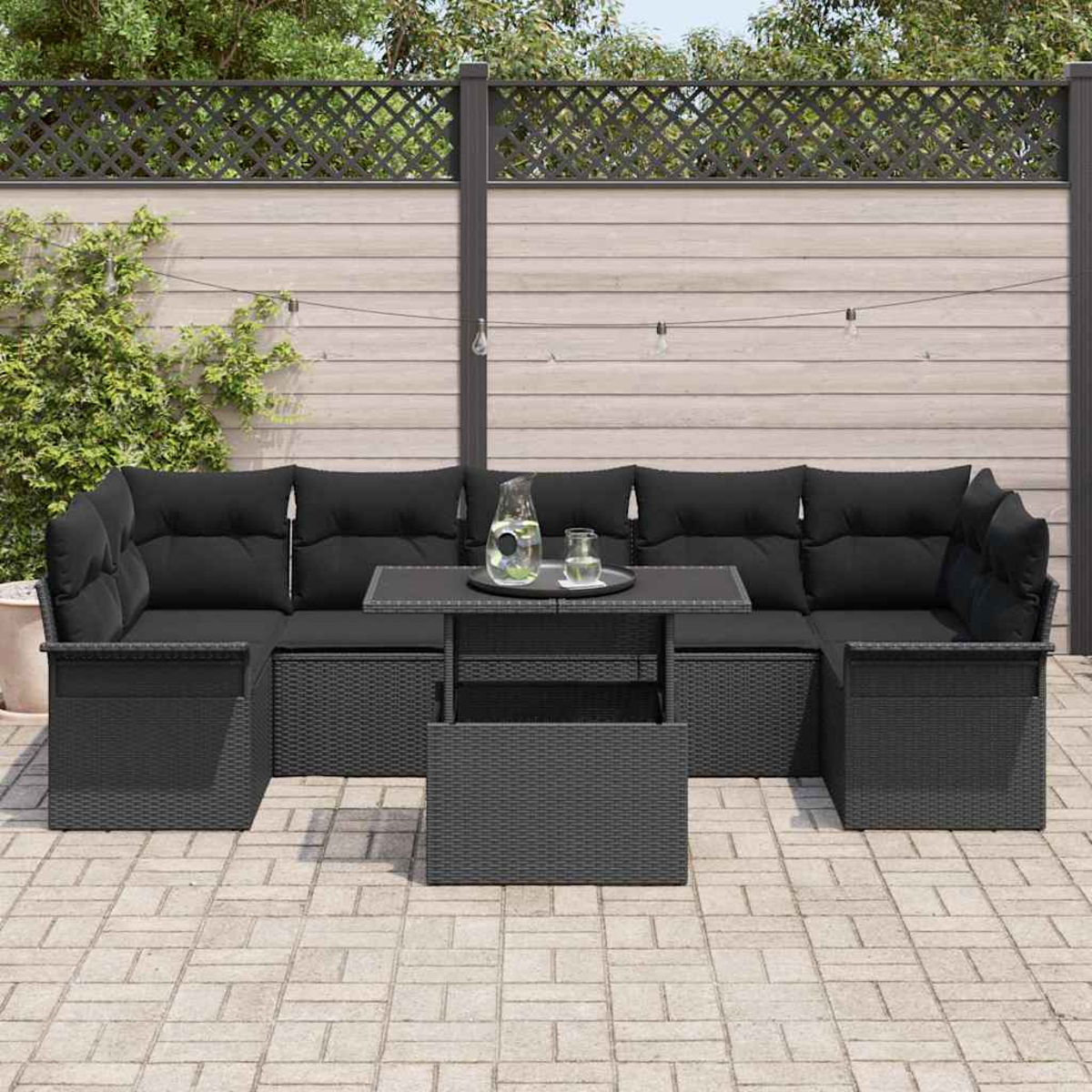 Schwarzes Outdoor-Ecksofa mit Kissen und einem Tisch auf einer Ziegelterrasse. Ein Zaun und Laub befinden sich im Hintergrund.