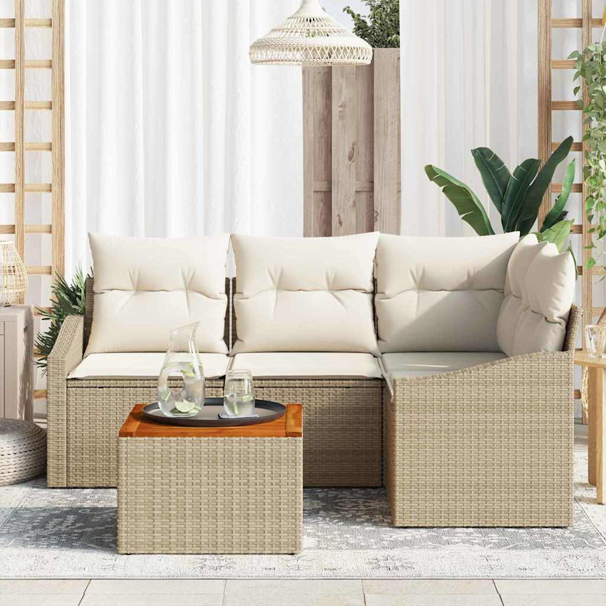 Ein beiges Rattan-Gartenmöbelset mit weißen Kissen steht auf einem Teppich, mit einem Krug und einem Glas auf einem Holztisch.