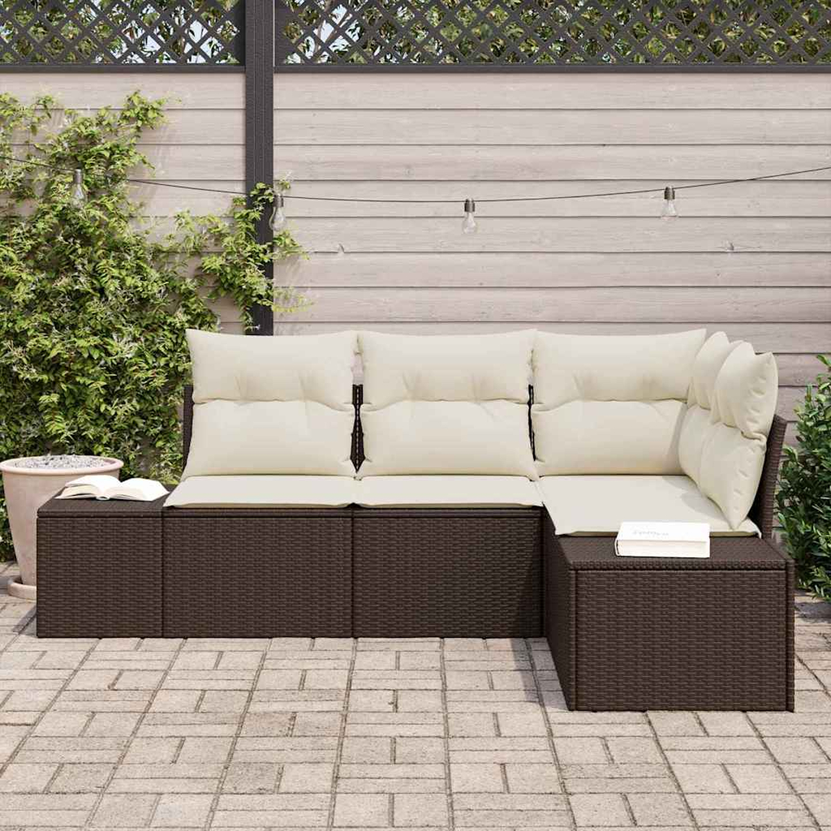 Ein braunes Outdoor-Ecksofa aus Korbgeflecht mit cremefarbenen Kissen steht auf einer Backstein-Terrasse. Im Hintergrund befinden sich ein Zaun und Pflanzen.