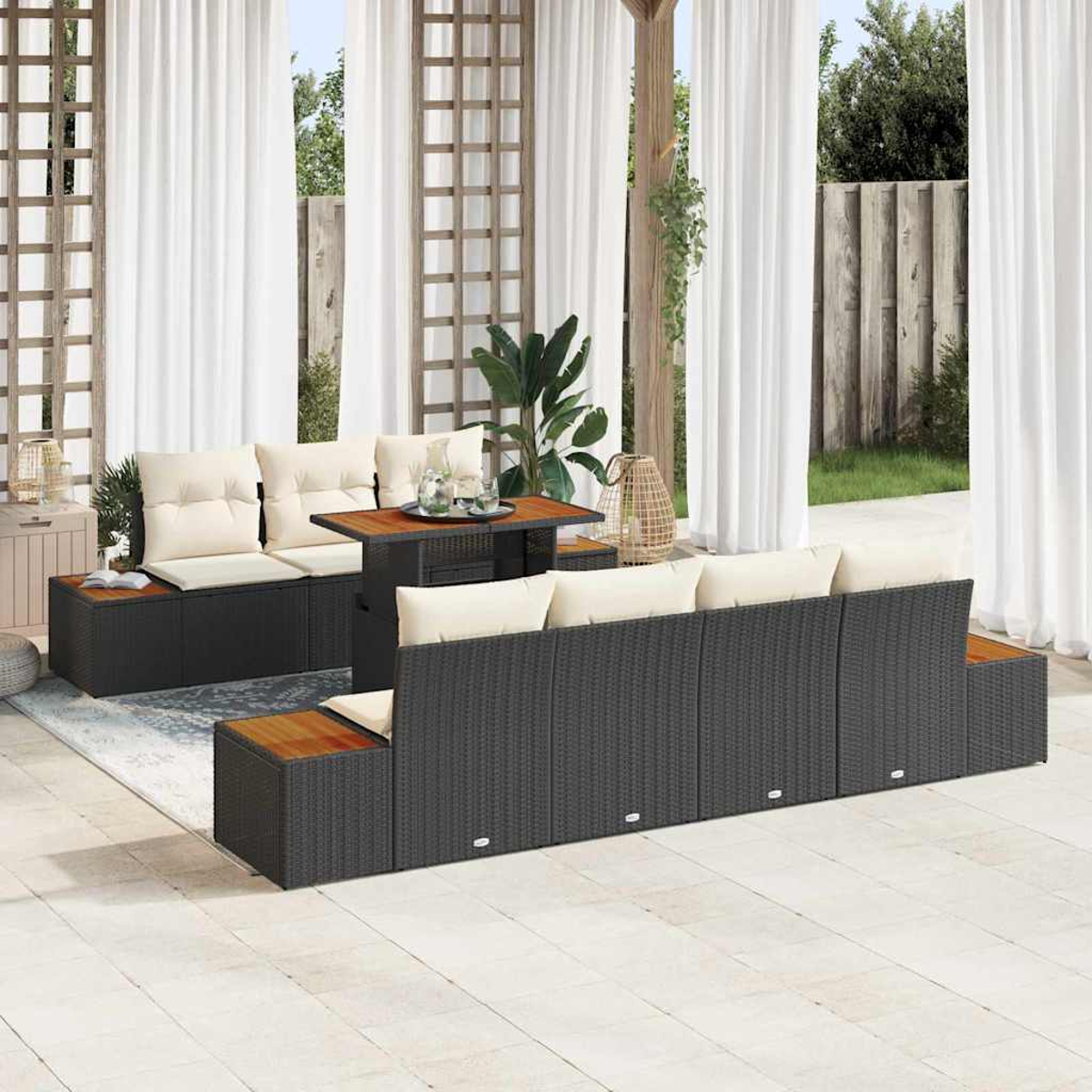 Terrassenset mit schwarzem Korbmöbel, cremefarbenen Kissen, Holztisch, weißen Vorhängen und Pflanzen.