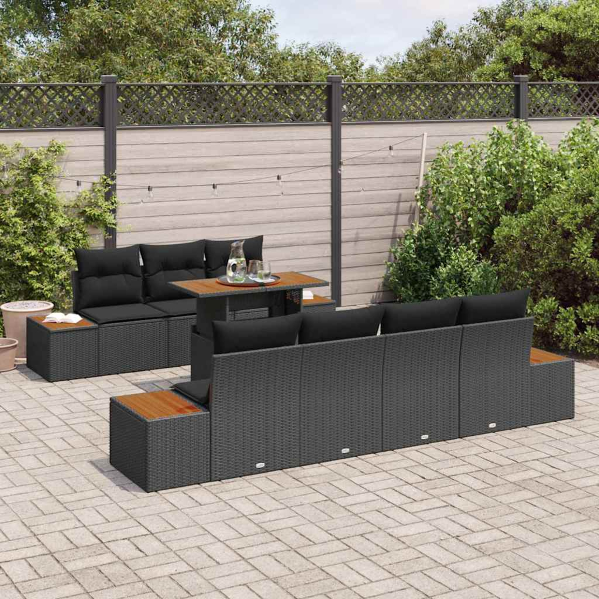 Gartenmöbel-Set mit Tisch, Sofas und Kissen. Im Hintergrund ein Gartenzaun und Grün.