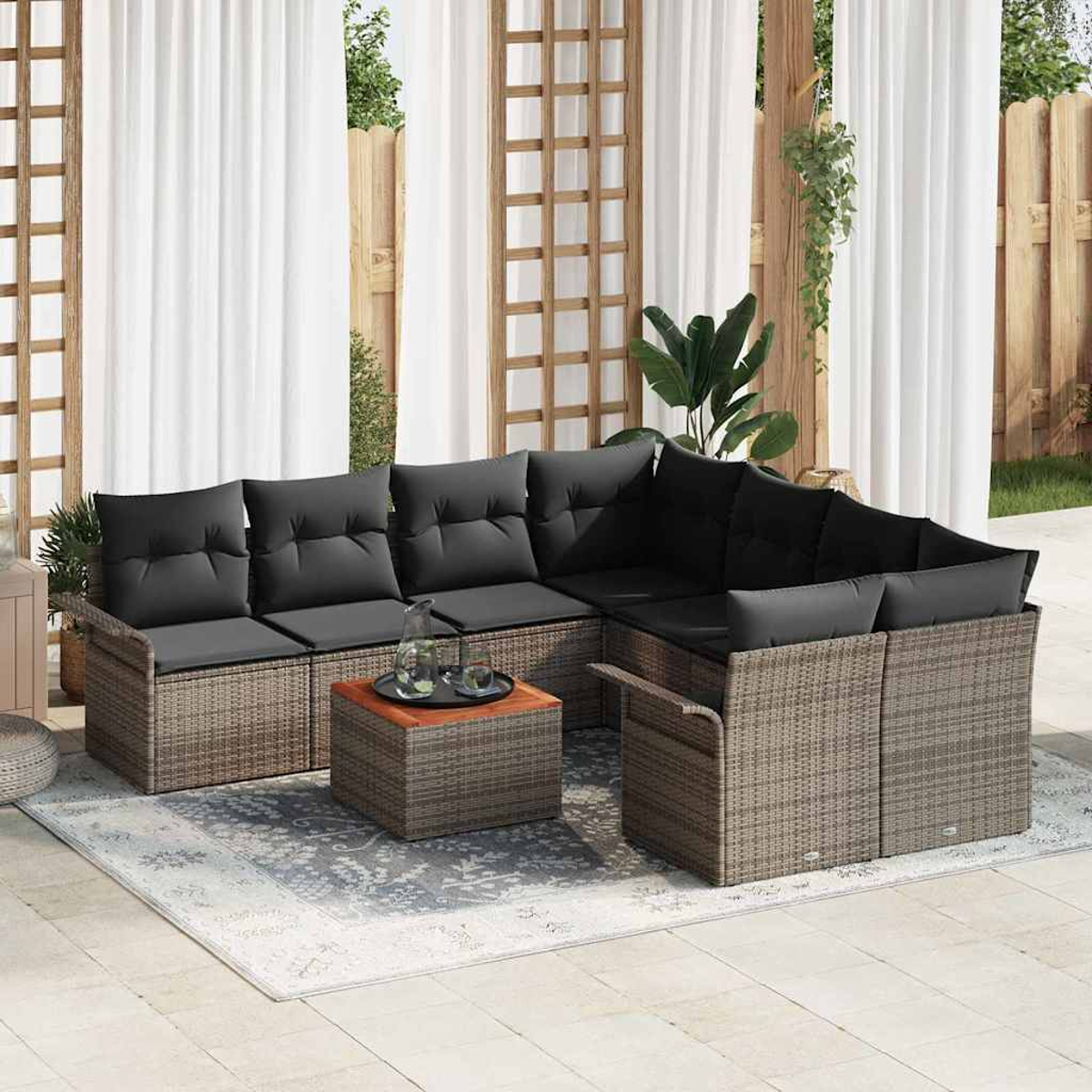 Outdoor-Ecksofa mit schwarzen Kissen, einem Couchtisch mit Getränken und einem Teppich. Der Hintergrund zeigt Vorhänge und einen Holzzaun.
