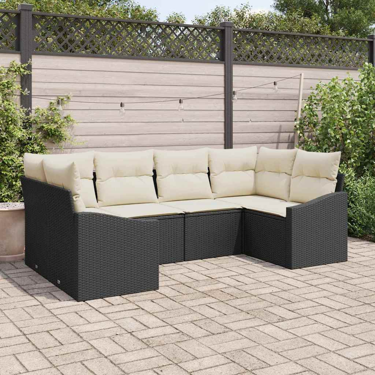 Ein schwarzes Outdoor-Ecksofa aus Korbgeflecht mit cremefarbenen Kissen steht auf einer Ziegelterrasse. Ein Zaun und Grünzeug befinden sich hinter dem Sofa.