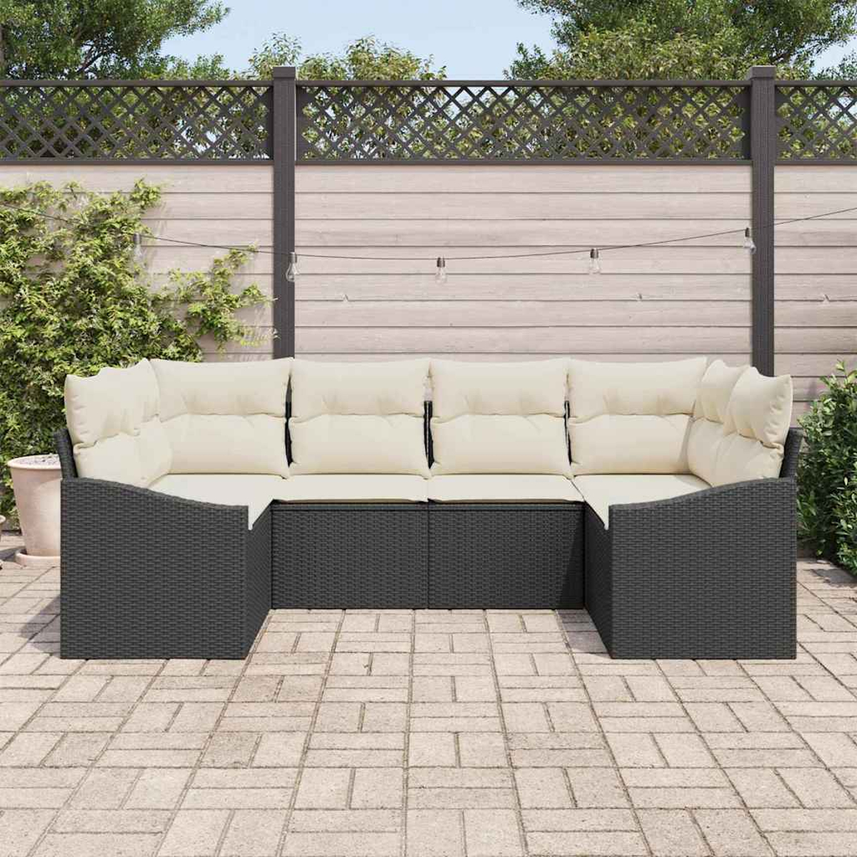 Ein dunkelgraues Outdoor-Ecksofa mit cremefarbenen Kissen steht auf einer Steinterrasse. Im Hintergrund befinden sich ein Holzzaun und Grün.