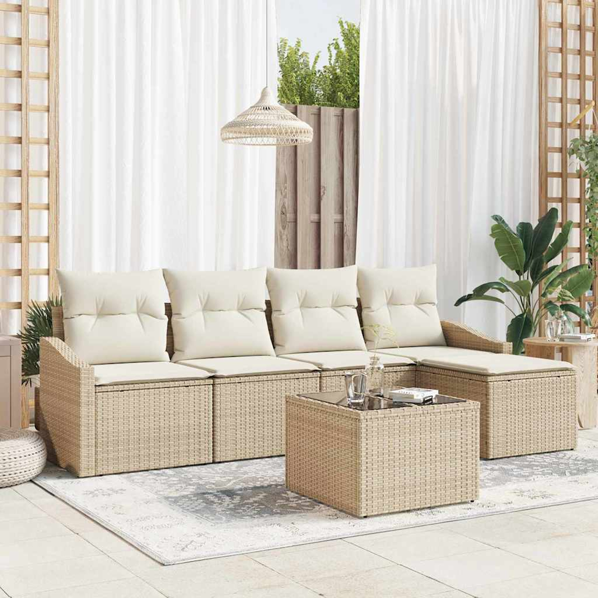Ein Korbmöbel mit cremefarbenen Kissen und einem passenden Couchtisch. Ein Teppich und Vorhänge sind im Hintergrund, zusammen mit Pflanzen.