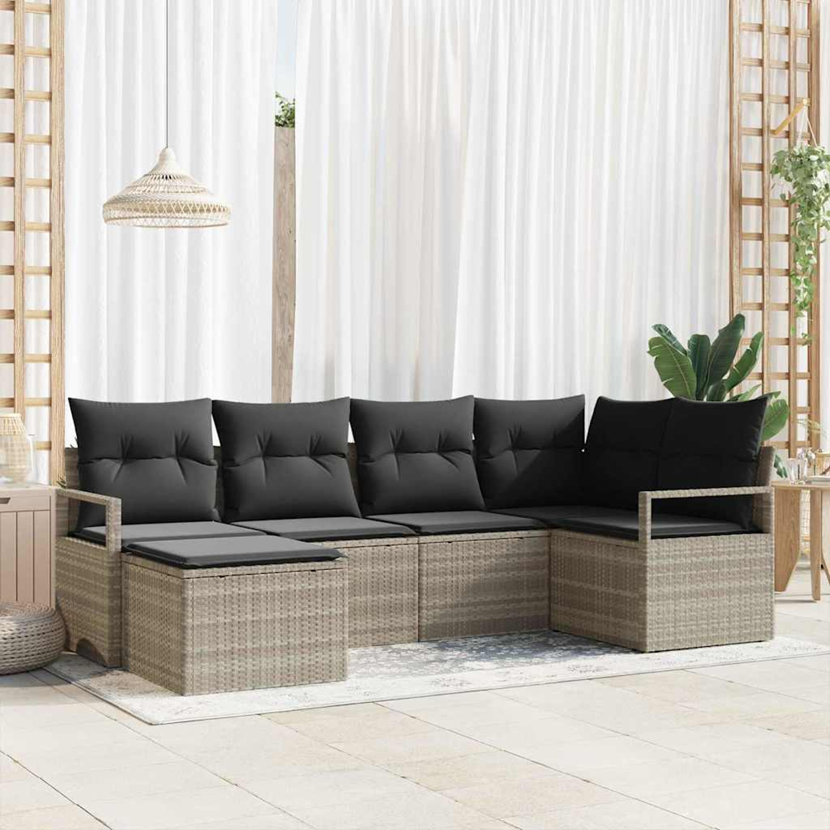 Geflochtenes Outdoor-Ecksofa mit schwarzen Kissen. Weiße Vorhänge im Hintergrund. Eine Hängelampe und Pflanzen sind sichtbar.