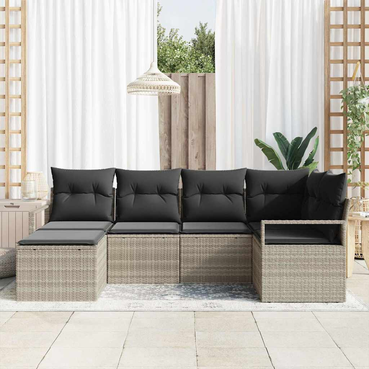 Geflochtenes Outdoor-Ecksofa mit schwarzen Kissen. Weiße Vorhänge, ein Fenster mit Grün und eine Hängelampe sind sichtbar.