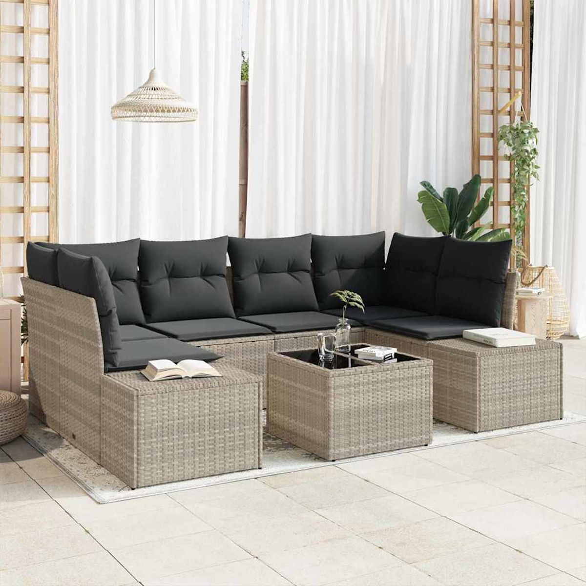 Sofá seccional exterior con cojines grises y marco estilo ratán. Mesa de centro con libros, planta y lámpara colgante tejida.