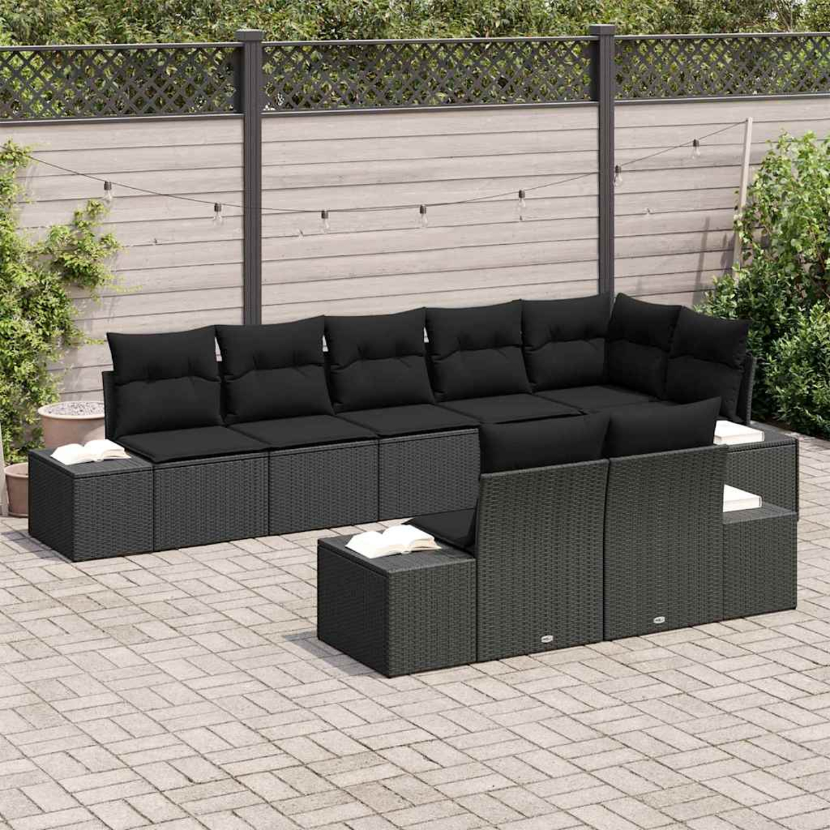 Outdoor-Ecksofa mit schwarzen Kissen. Bücher liegen auf den Beistelltischen. Der Hintergrund zeigt einen Holzzaun und Grün.
