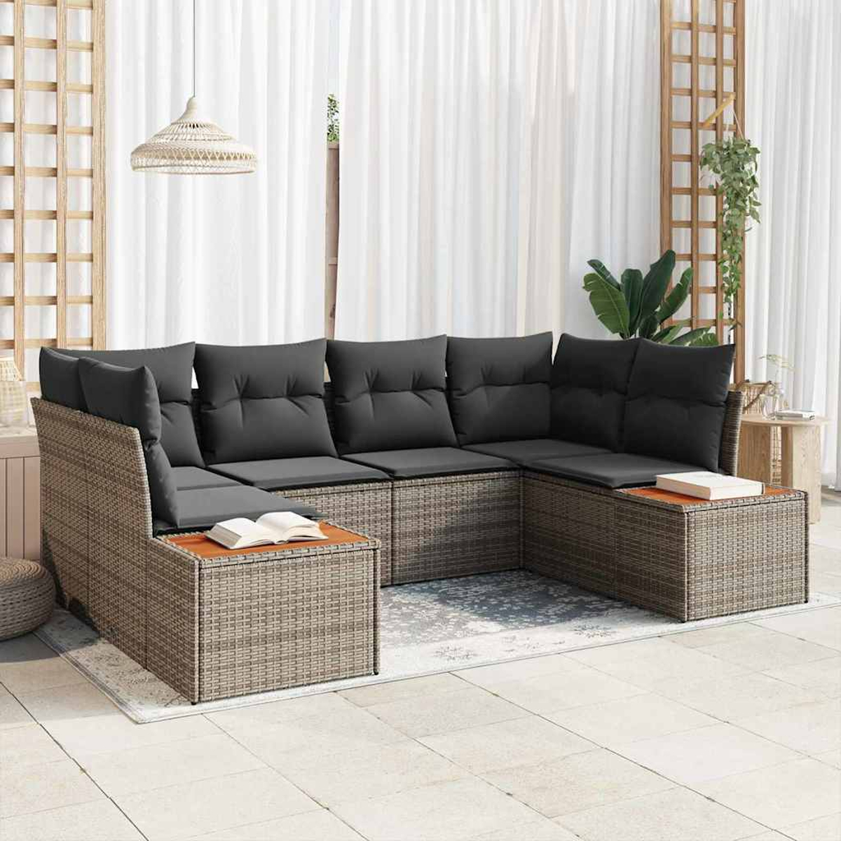 Outdoor-Ecksofa mit grauen Kissen und gewebtem Rahmen. Bücher auf Beistelltischen. Weiße Vorhänge und eine Hängelampe im Hintergrund.