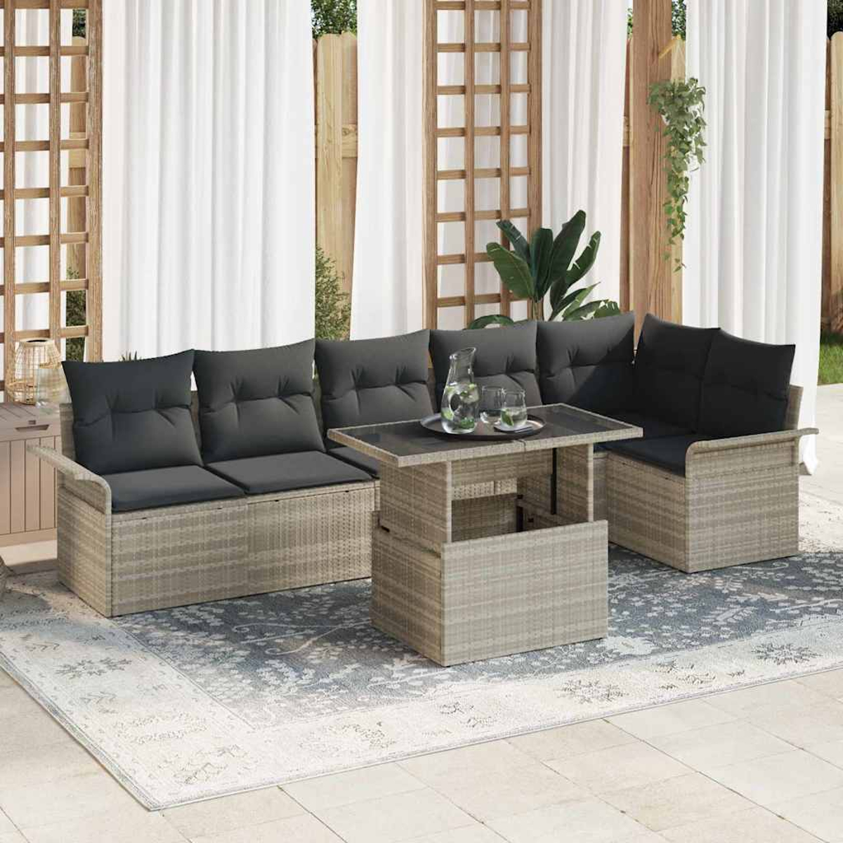 Terrassenset im Freien mit grauen Kissen, einem Tisch mit Glasplatte und einem Teppich. Weiße Vorhänge und Holzgitter im Hintergrund.