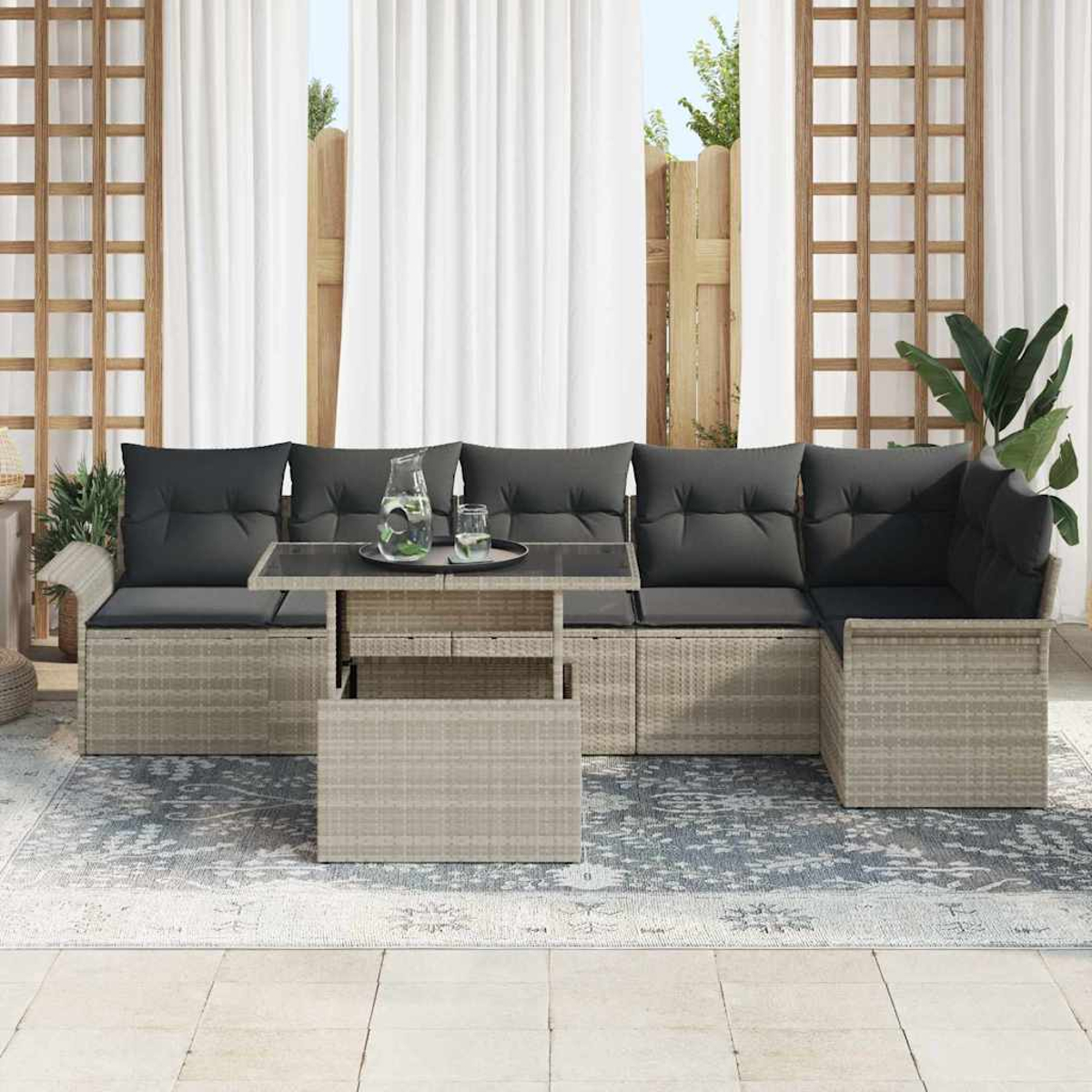Szene im Freien mit grau gepolstertem Sofaset, Glastisch mit Getränken und einem gemusterten Teppich. Weiße Vorhänge und Holzzaun im Hintergrund.