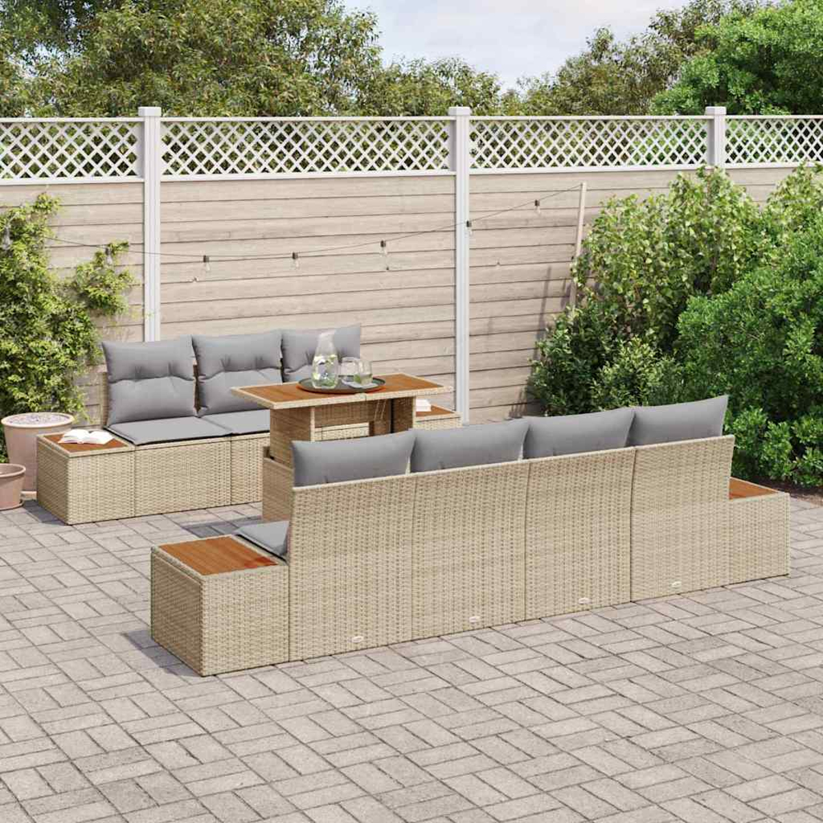 Gartenmöbel-Set aus Korbgeflecht mit grauen Kissen, einem Holztisch und einem Gitterzaun auf einer gepflasterten Terrasse.