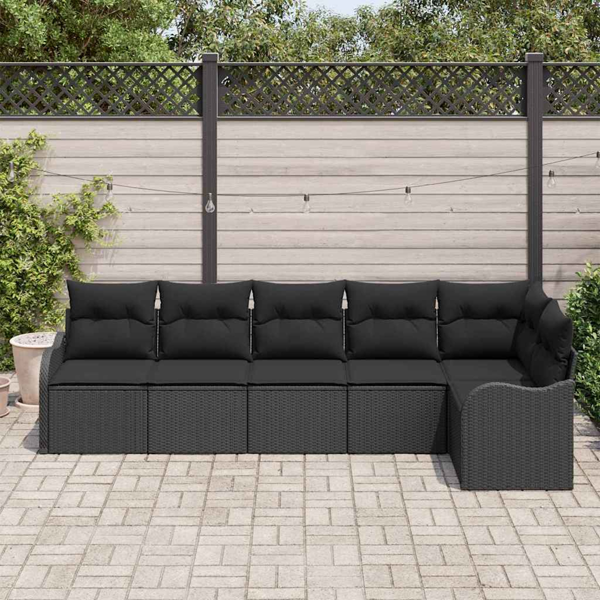 Outdoor-Ecksofa mit schwarzen Kissen auf einer Terrasse. Im Hintergrund sind ein Zaun und Grün zu sehen. Lichterketten sind gespannt.