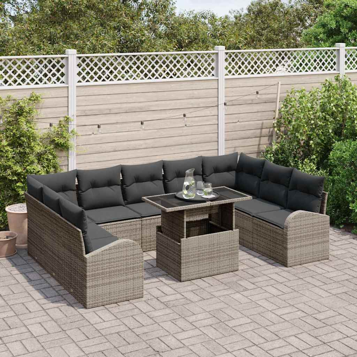 Gartenmöbel-Set mit grauen Kissen, einem Tisch mit Glaskrug und einem weißen Zaun im Hintergrund.