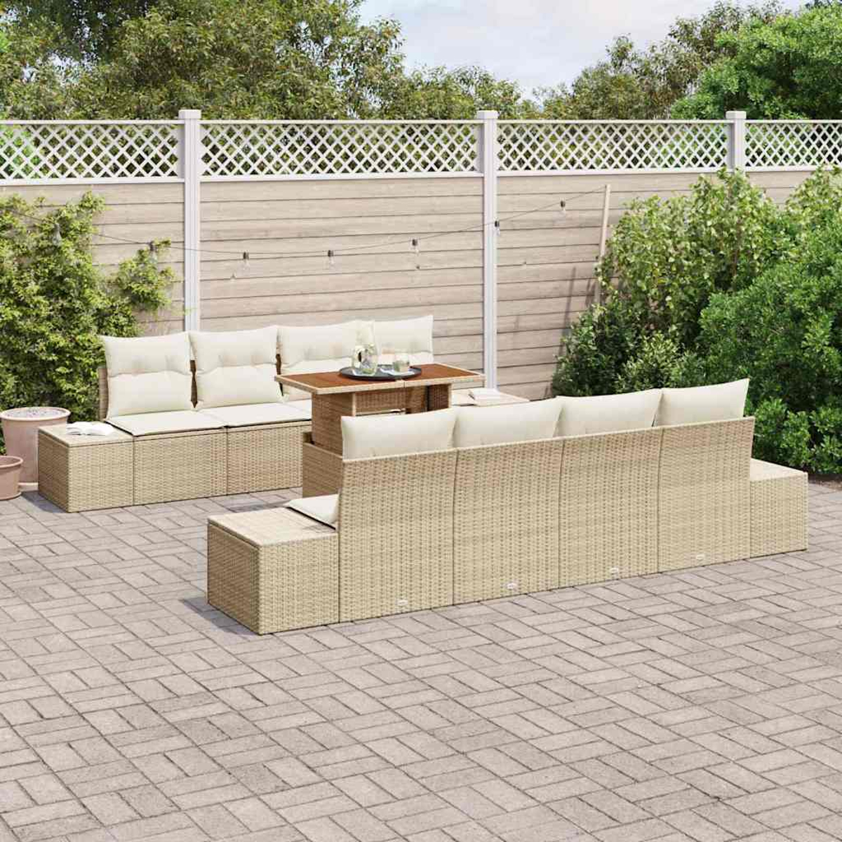 Gartenmöbel-Set aus Korbgeflecht mit cremefarbenen Kissen auf einer Steinterrasse. Ein Holztisch und ein weißer Zaun im Hintergrund.