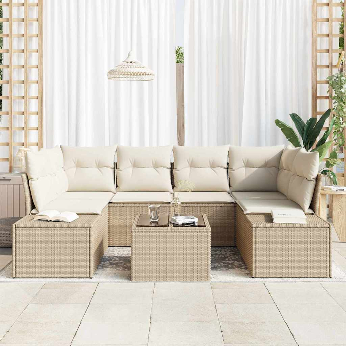 Un sofá exterior de mimbre beige con cojines crema y una mesita. Cortinas blancas en el fondo.