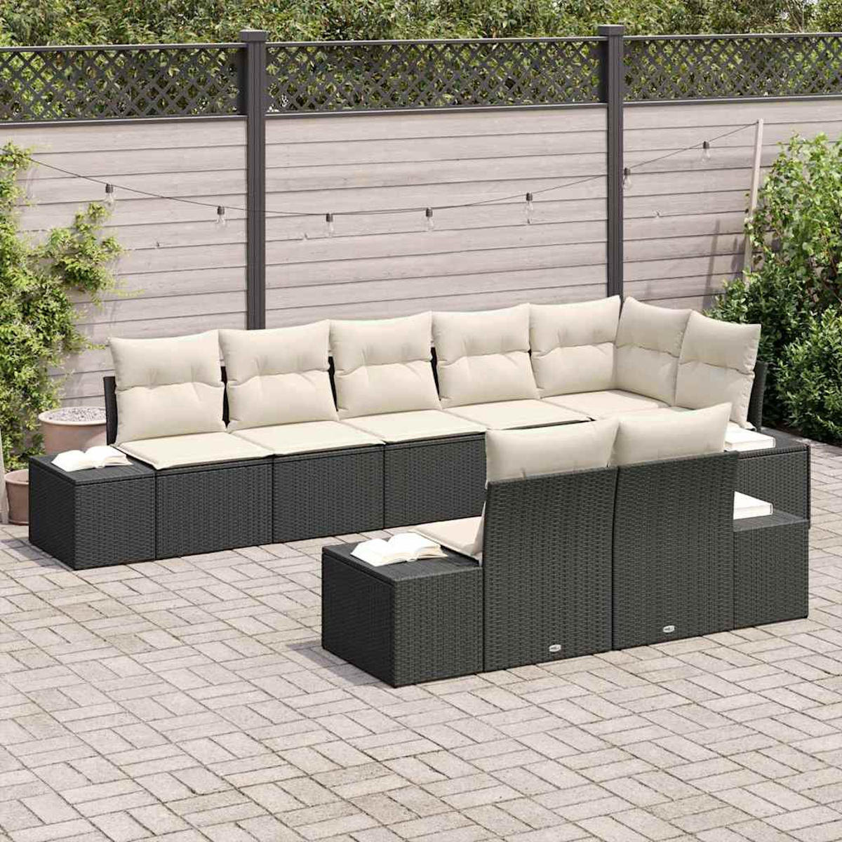 Outdoor-Ecksofa mit beigen Kissen auf einer gepflasterten Terrasse. Ein Zaun und Grünzeug sind im Hintergrund. Bücher liegen auf dem Sofa.