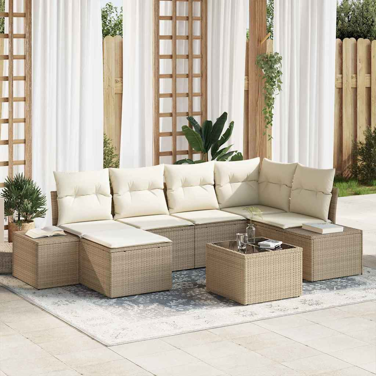 Divano componibile da esterno con cuscini color crema e base intrecciata. Tavolino, tappeto, tende e traliccio in legno sullo sfondo.