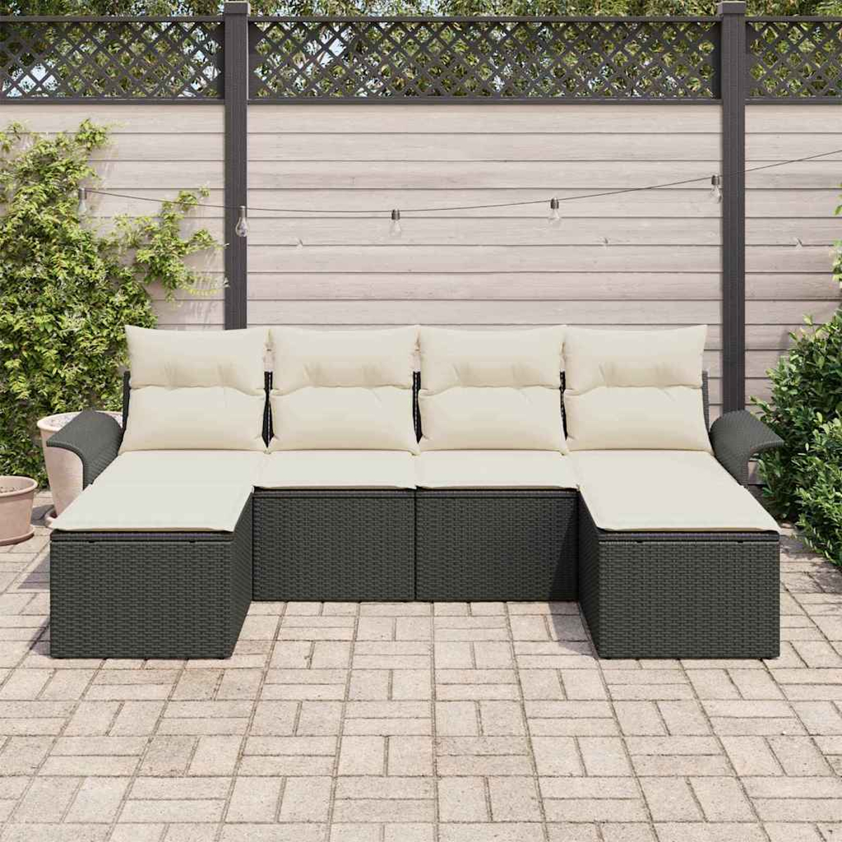 Dunkelgraues Outdoor-Ecksofa mit cremefarbenen Kissen auf einer Backstein-Terrasse. Ein Holzzaun und Grünzeug sind im Hintergrund.