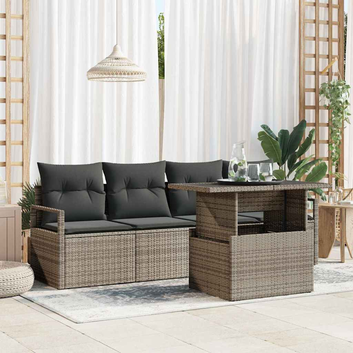Terrassenset mit Sofa, Tisch und Pflanzen. Graue Kissen, gewebte Möbel und weiße Vorhänge schaffen ein entspanntes Ambiente.