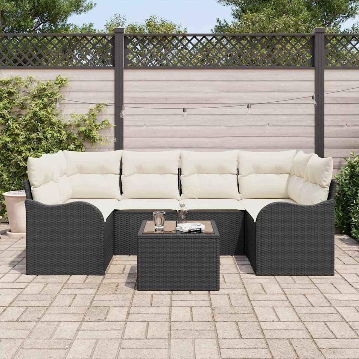 Outdoor-Ecksofa mit cremefarbenen Kissen und einem kleinen Tisch. Im Hintergrund befinden sich ein Holzzaun und Grün.