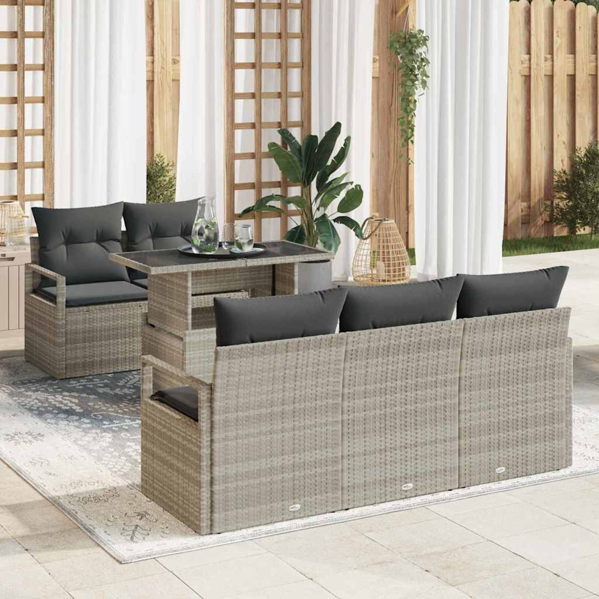 Gartenmöbel-Set mit grauen Kissen und Tisch. Im Hintergrund Vorhänge, Pflanzen und Holzzaun.