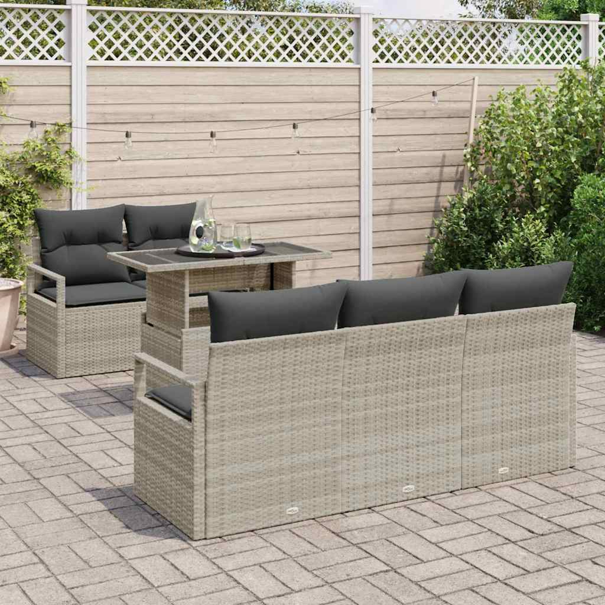 Garten-Terrassengarnitur: Hellbraunes Korbmöbel-Sofa und Stuhl mit grauen Kissen, Tisch mit Getränken und weißem Gitterzaun im Hintergrund.