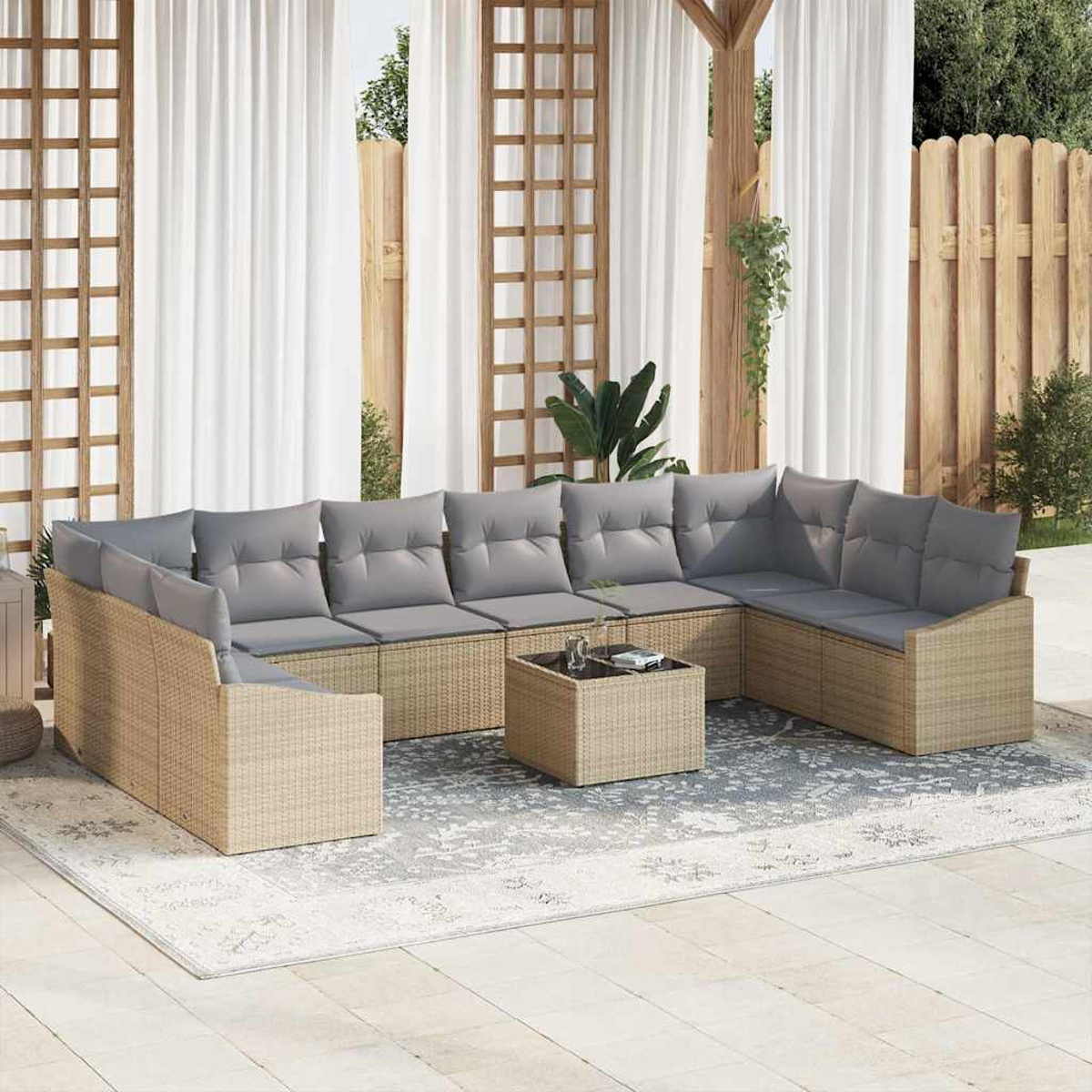 Außensofa mit grauen Kissen auf einer Terrasse mit Teppich und Couchtisch. Transparente Vorhänge und Holzzaun im Hintergrund.