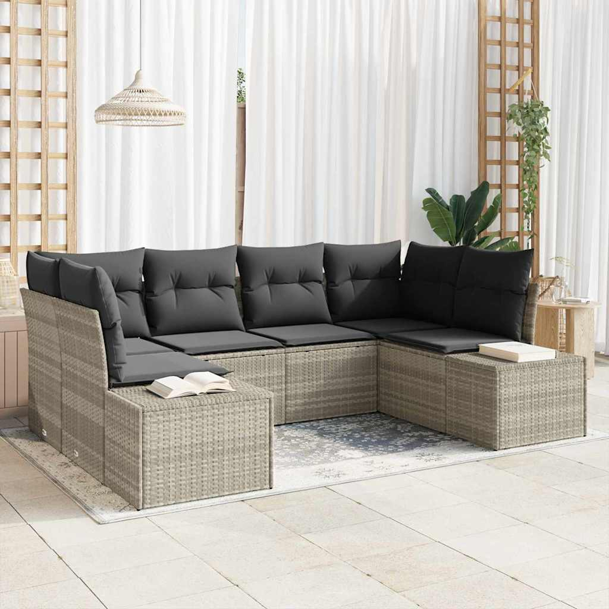 Outdoor-Ecksofa mit grauen Kissen, Büchern und einer gewebten Lampe. Auf einem Teppich, mit weißen Vorhängen und einem Holzgitter im Hintergrund.