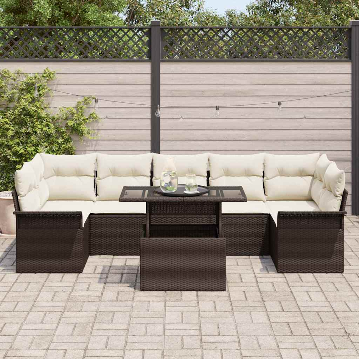 Outdoor-Rattan-Sofagarnitur mit cremefarbenen Kissen und Glastisch. Auf einer Terrasse mit Zaun und Lichterketten im Hintergrund.
