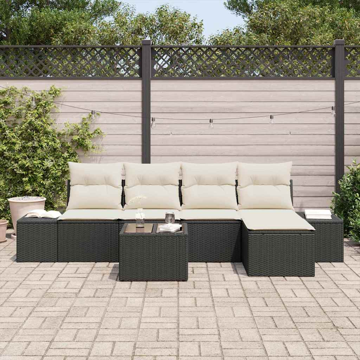 Outdoor-Ecksofa mit cremefarbenen Kissen und kleinem Tisch auf einer Ziegelterrasse. Hintergrund ist ein Zaun und Pflanzen.