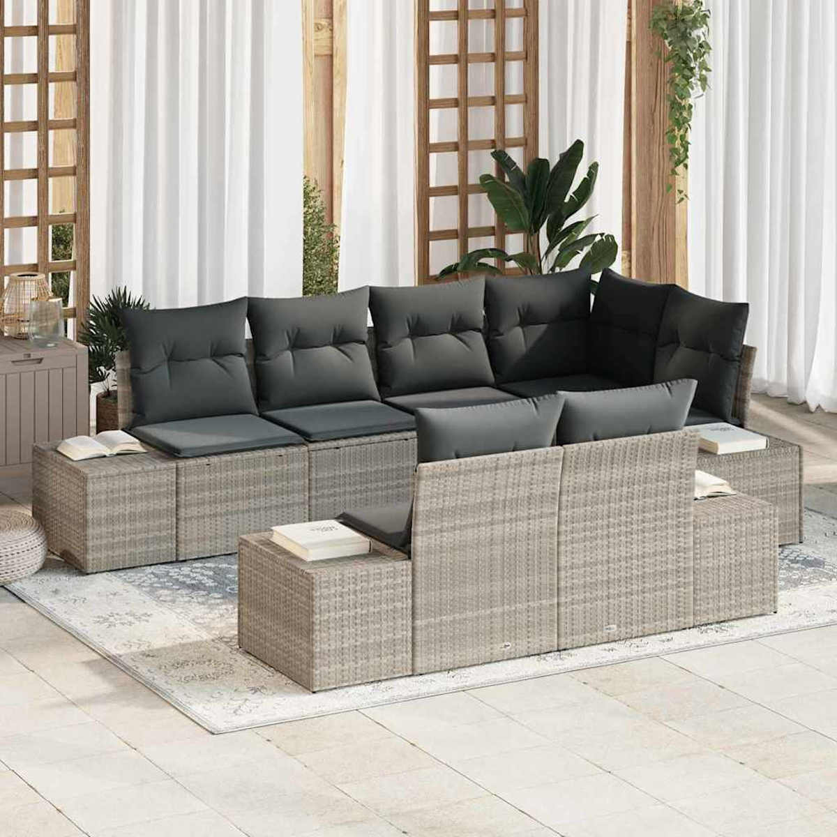 Graues Outdoor-Ecksofa aus Korbgeflecht mit dunkelgrauen Kissen. Bücher an den Seiten. Weiße Vorhänge im Hintergrund.