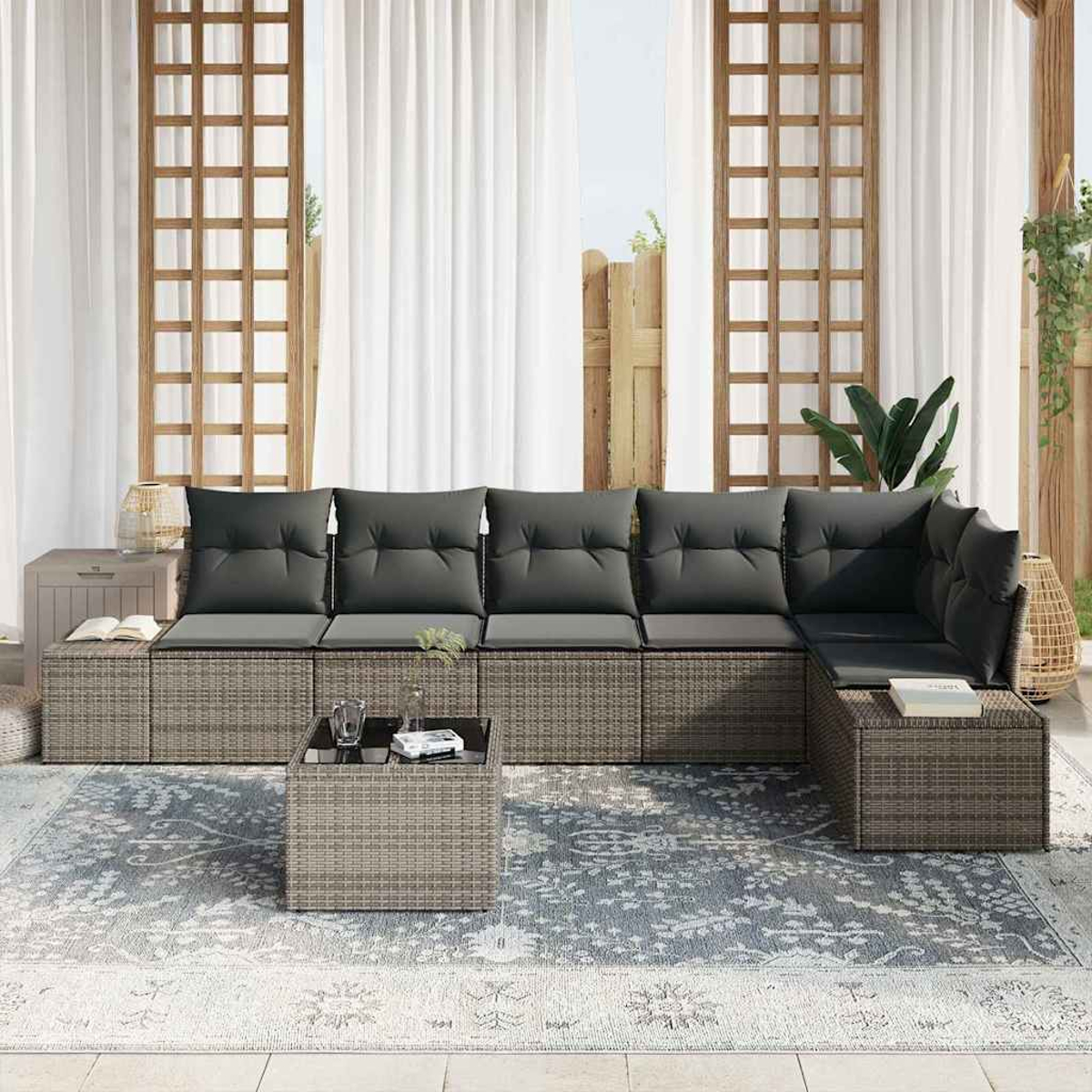 Outdoor-Ecksofa mit grauen Kissen und einem Couchtisch auf einem gemusterten Teppich vor weißen Vorhängen.