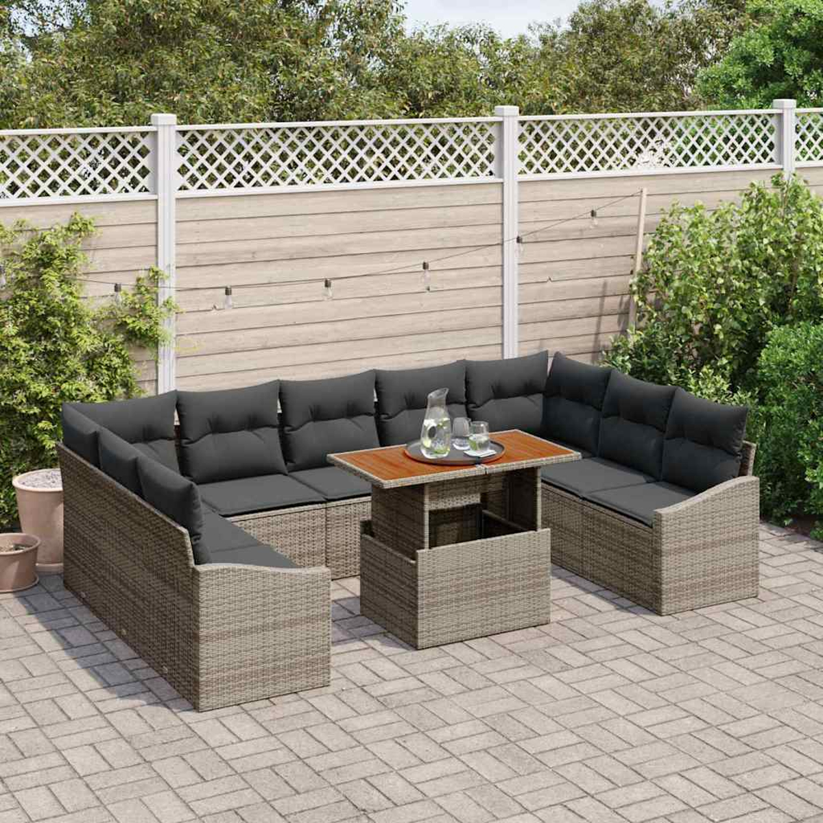 Garten-Terrassenset mit grauen Kissen und einem Holztisch. Weißer Zaun und Grün in der Hintergrund. Gepflasterter Boden.