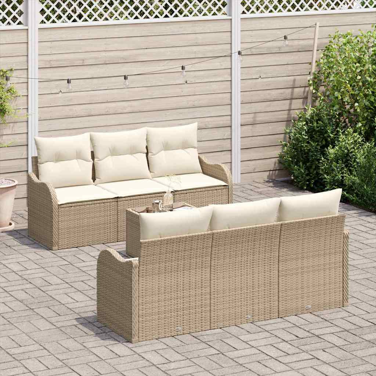 Zwei Korbmöbel-Sofas mit cremefarbenen Kissen auf einer gepflasterten Terrasse. Ein kleiner Tisch steht dazwischen. Ein weißer Gitterzaun ist im Hintergrund.