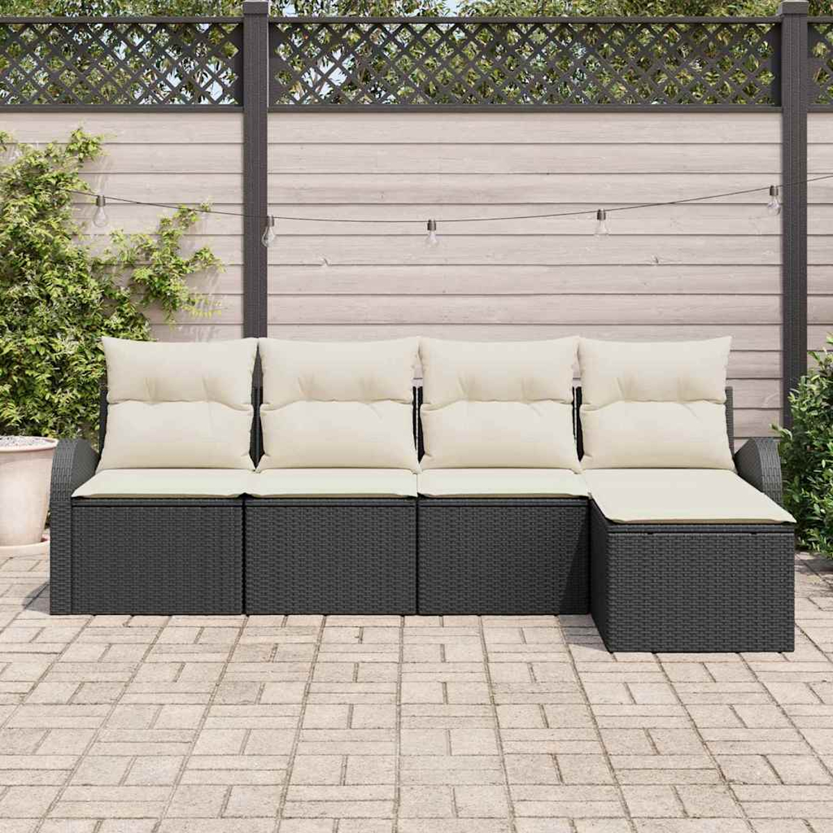 Outdoor-Sofa mit schwarzem, gewebtem Untergestell, cremefarbenen Kissen und Rückenlehnen. Auf einer gepflasterten Terrasse, im Hintergrund ein Holzzaun.