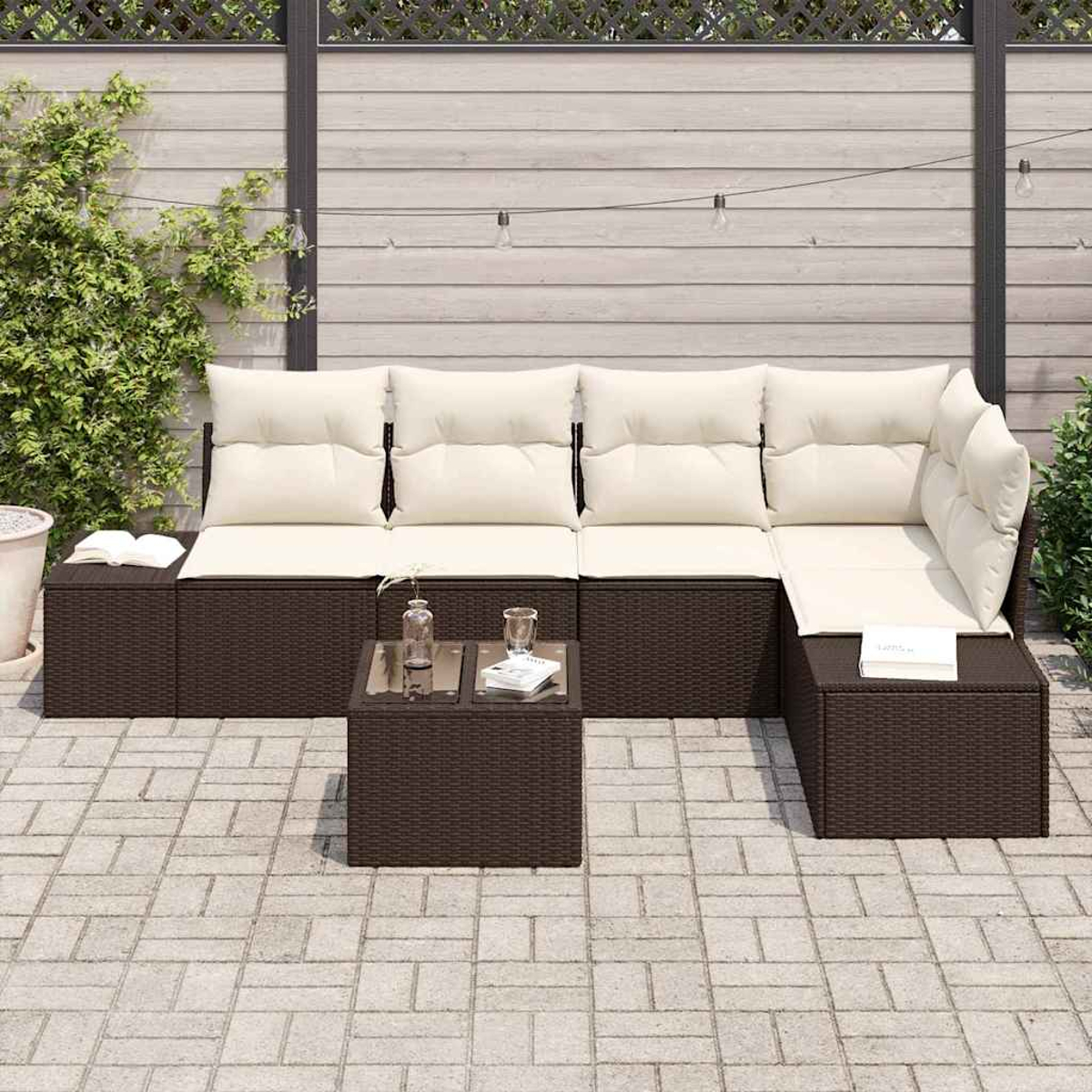 Sofá seccional exterior con cojines crema y una mesita. El fondo presenta una valla de madera, plantas y un patio de ladrillos.