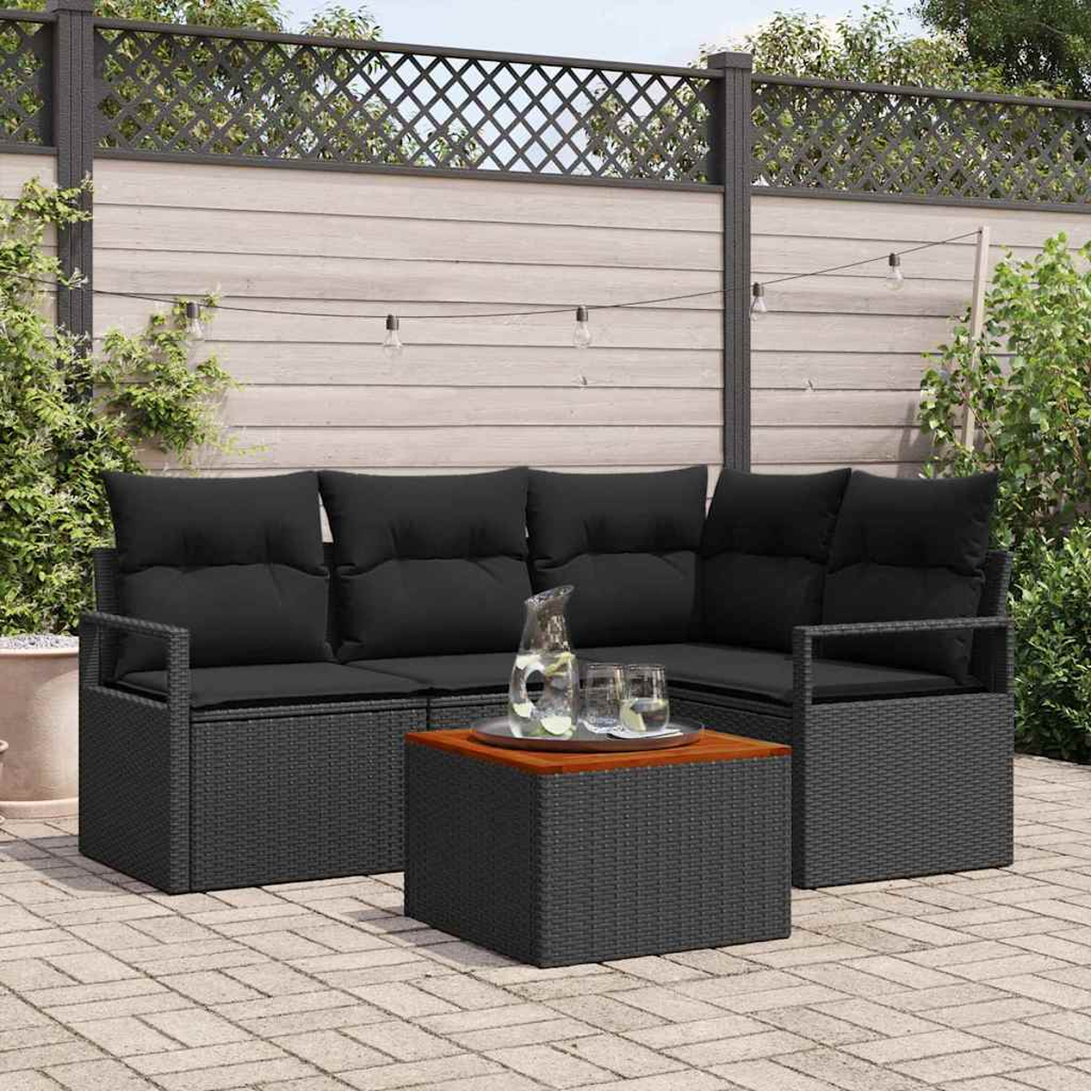 Gartenmöbel. Schwarzes Korbsessel und Couchtisch mit Holzplatte. Kanne und Gläser stehen auf dem Tisch.