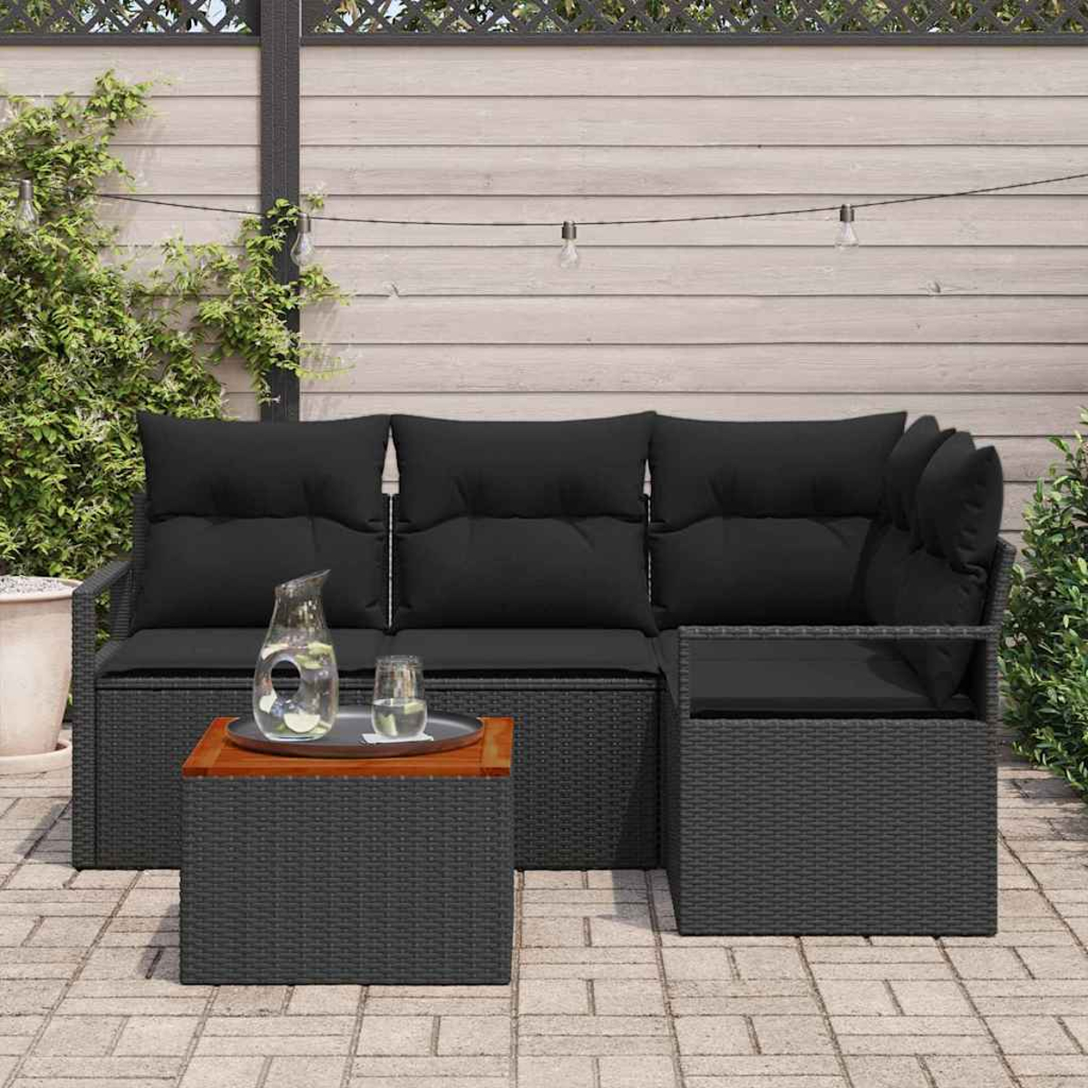 Gartenset mit schwarzem Korbmöbel und Couchtisch. Auf dem Tisch stehen ein Krug und Gläser. Der Hintergrund hat Holzverkleidung.