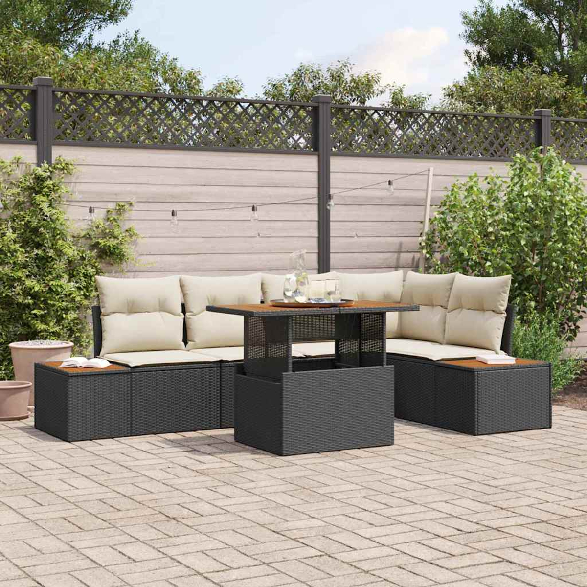 Terrassenmöbel-Set mit schwarzem Korbmöbeln, beigen Kissen und einem Holztisch. Die Szene spielt sich vor einem Zaun und Grün ab.