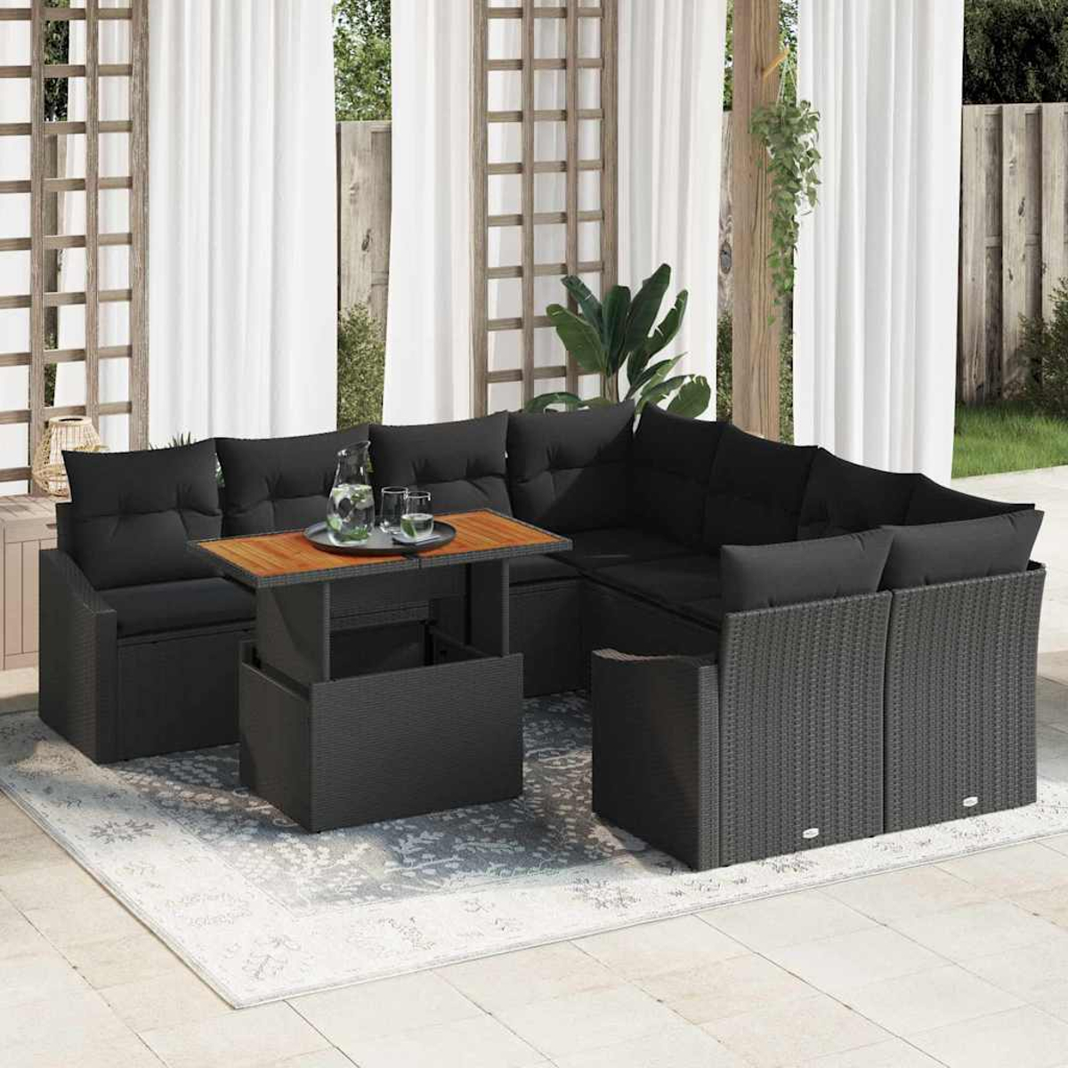 Outdoor-Ecksofa mit schwarzen Kissen und einem Holztisch, auf einem gemusterten Teppich. Vorhänge und eine Holzkonstruktion im Hintergrund.