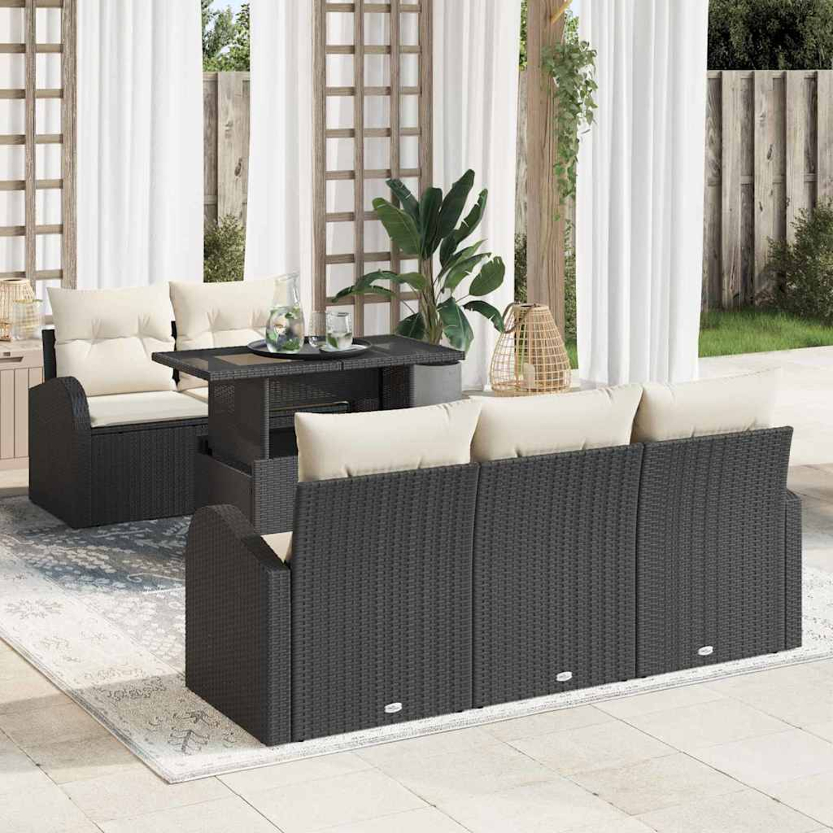 Juego de muebles de patio al aire libre con sofá gris oscuro, silla y mesa con cojines crema, sobre una alfombra. Cortinas blancas al fondo.