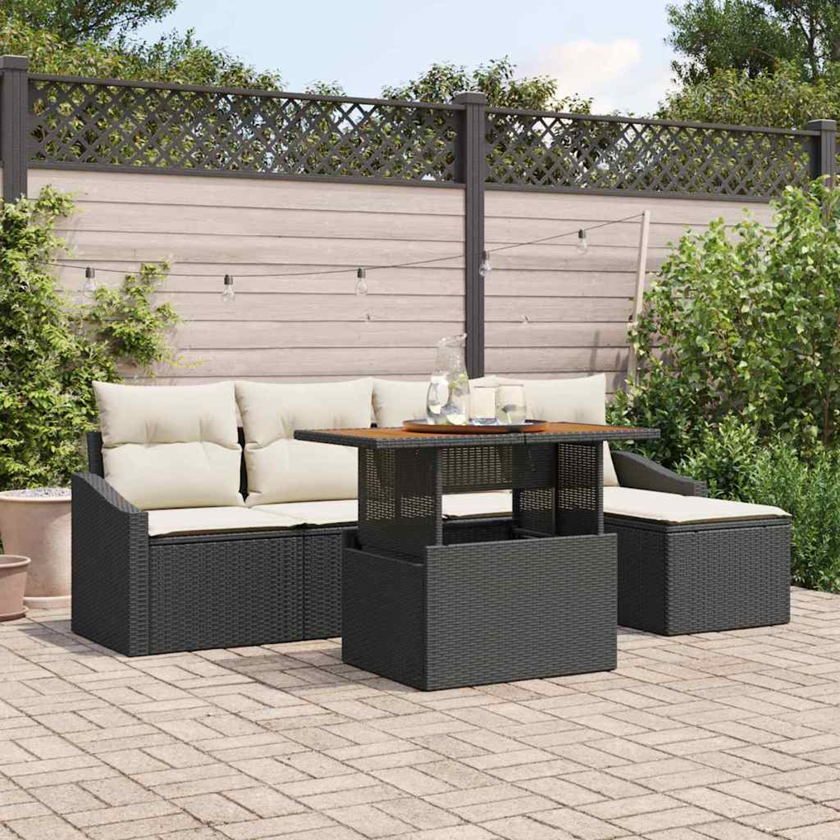 Garten-Terrassenset mit Sofa, Tisch und Ottomane. Beige Kissen und eine braune Tischplatte. Holzzaun im Hintergrund.