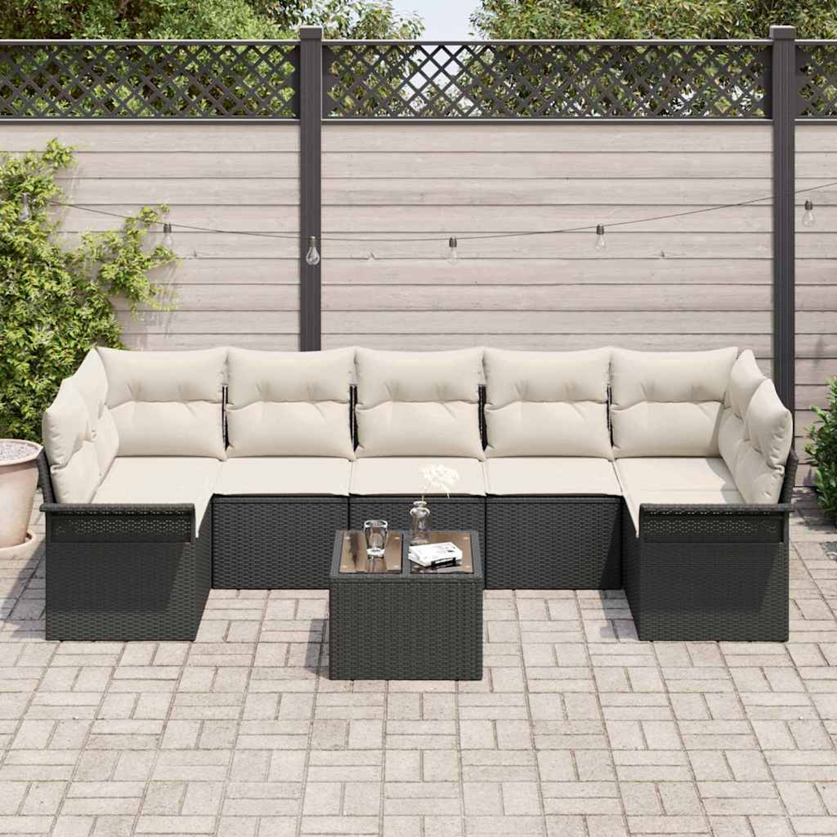 Garten-Terrassenset mit schwarzem Korbgeweberahmen, beigen Kissen und einem kleinen Tisch. Im Hintergrund ein Holzzaun.