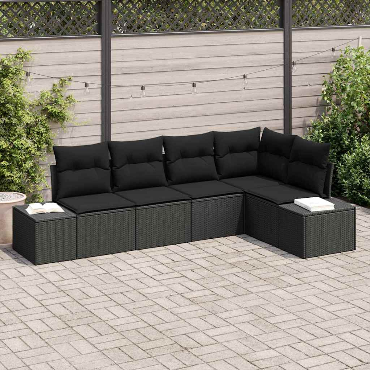 Ein Ecksofa im Freien mit schwarzen Kissen auf einer gepflasterten Terrasse, mit einem Holzzaun im Hintergrund.