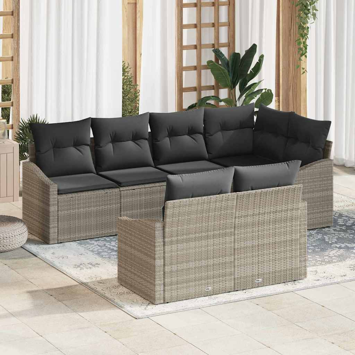 Outdoor-Korbsessel mit schwarzen Kissen. Die Szene umfasst einen Teppich, Vorhänge und Pflanzen für eine entspannte Atmosphäre.