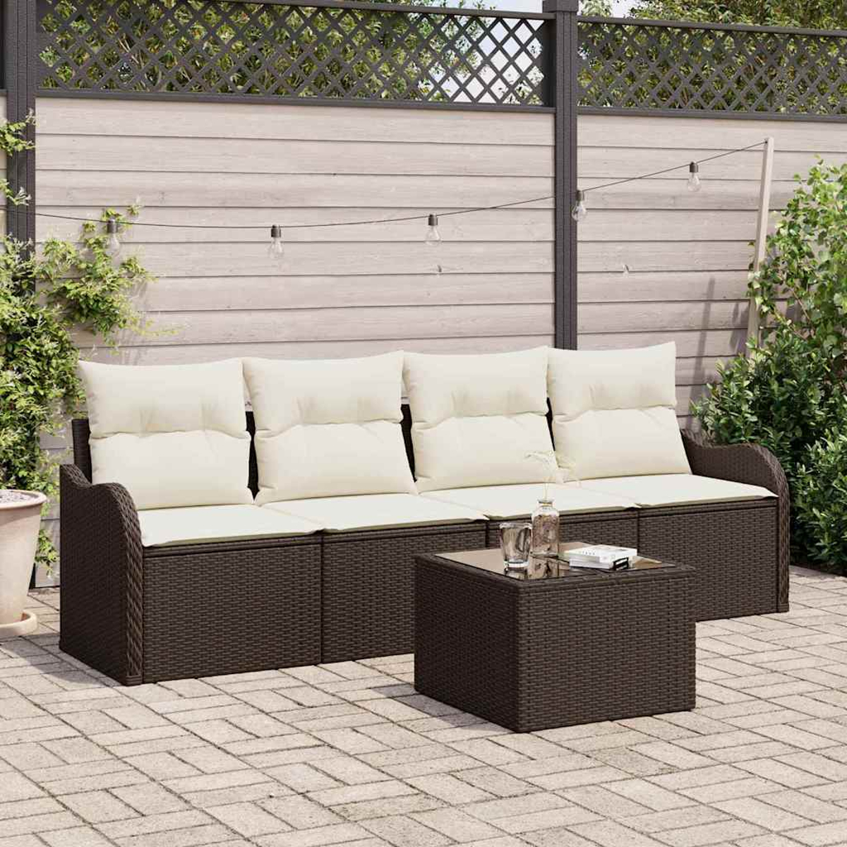 Ein braunes Korbmöbel mit cremefarbenen Kissen und ein passender Couchtisch stehen auf einer Terrasse. Im Hintergrund befindet sich ein Holzzaun.