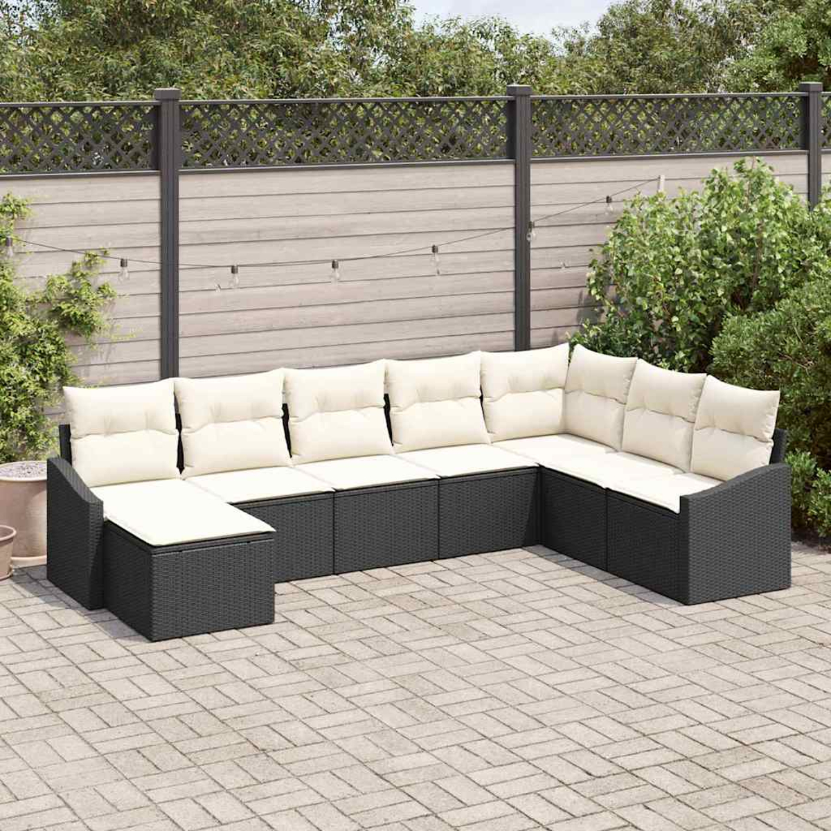 Ein Ecksofa im Freien mit weißen Kissen steht auf einer gepflasterten Terrasse. Ein Holzzaun und Grünzeug sind im Hintergrund.