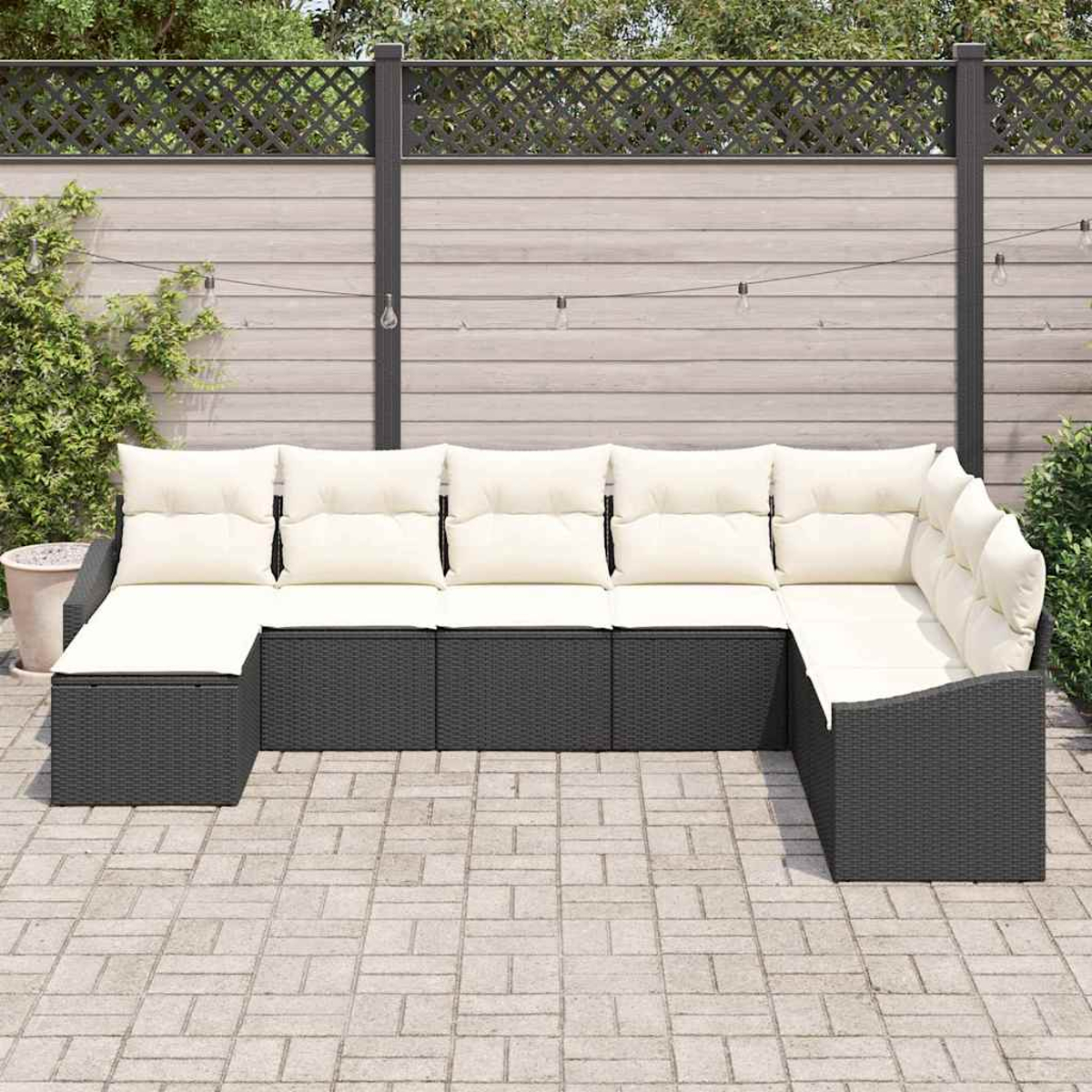 Graues Rattan-Ecksofa mit cremefarbenen Kissen. Es steht auf einer Steinterrasse mit Holzzaun und Grün in Hintergrund.